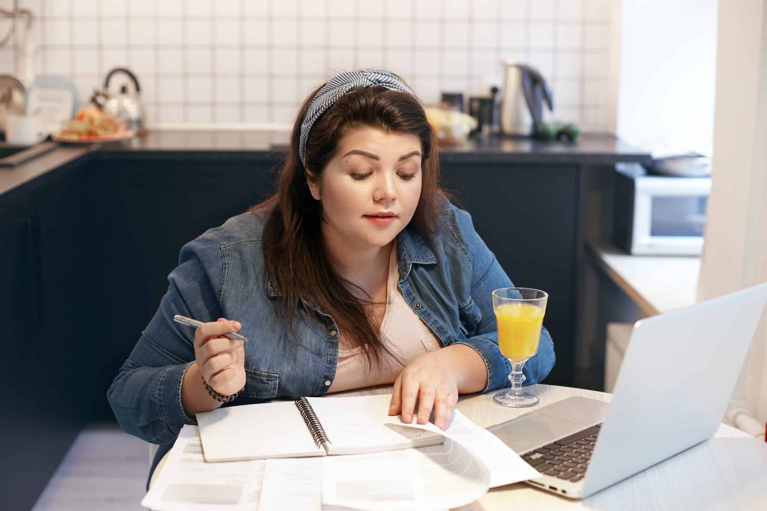 Ensino a distancia: aluna em sua mesa de estudos utilizando uma caneta para fazer anotações em um caderno enquanto estuda.