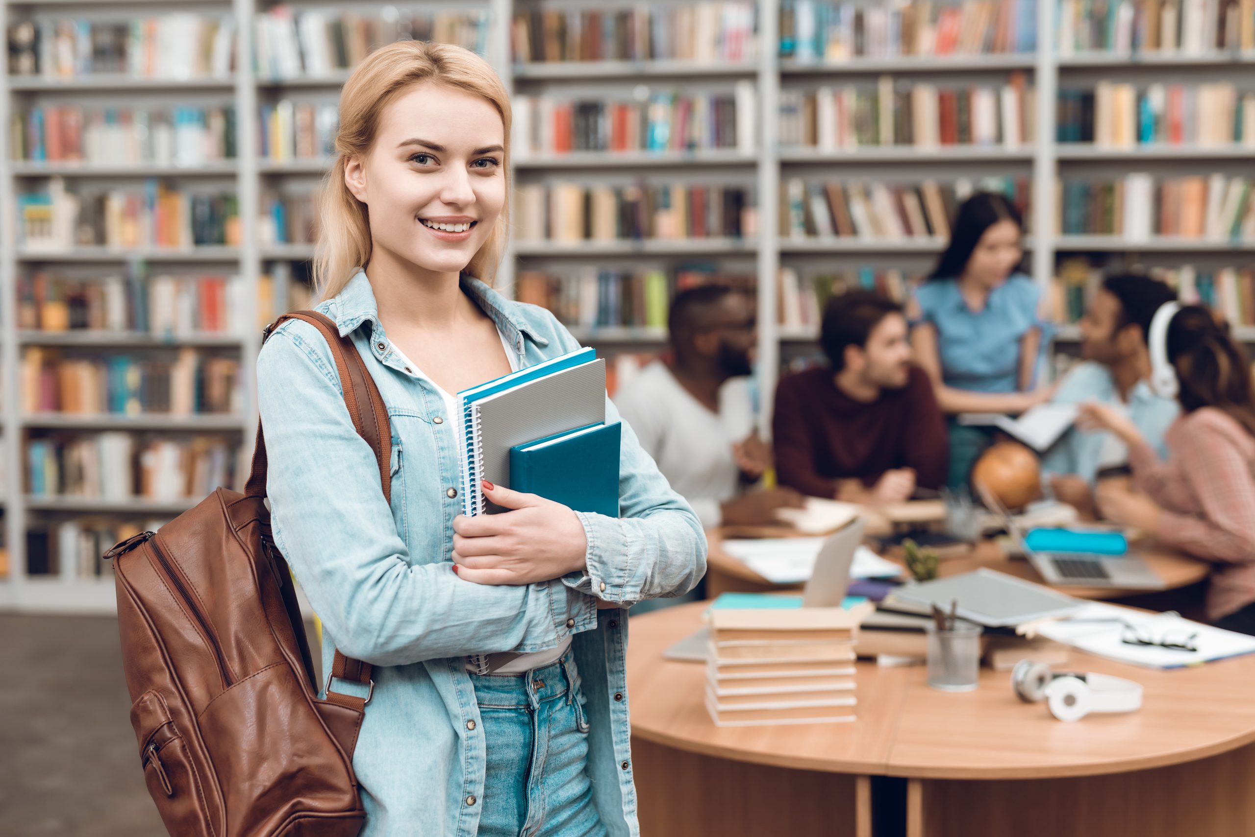Grupo de estudantes multiculturais étnicos sentado na biblioteca, com uma mulher a frente segurando livros
