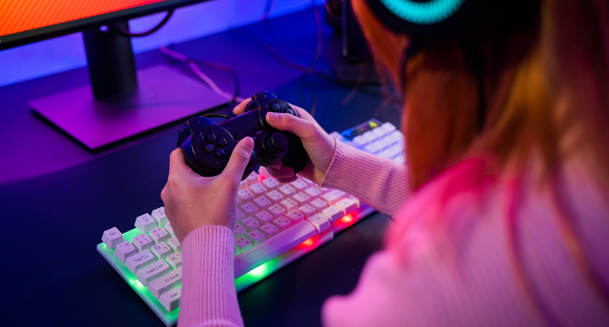 Mulher com fones de ouvido e um console em frente a um computador.
