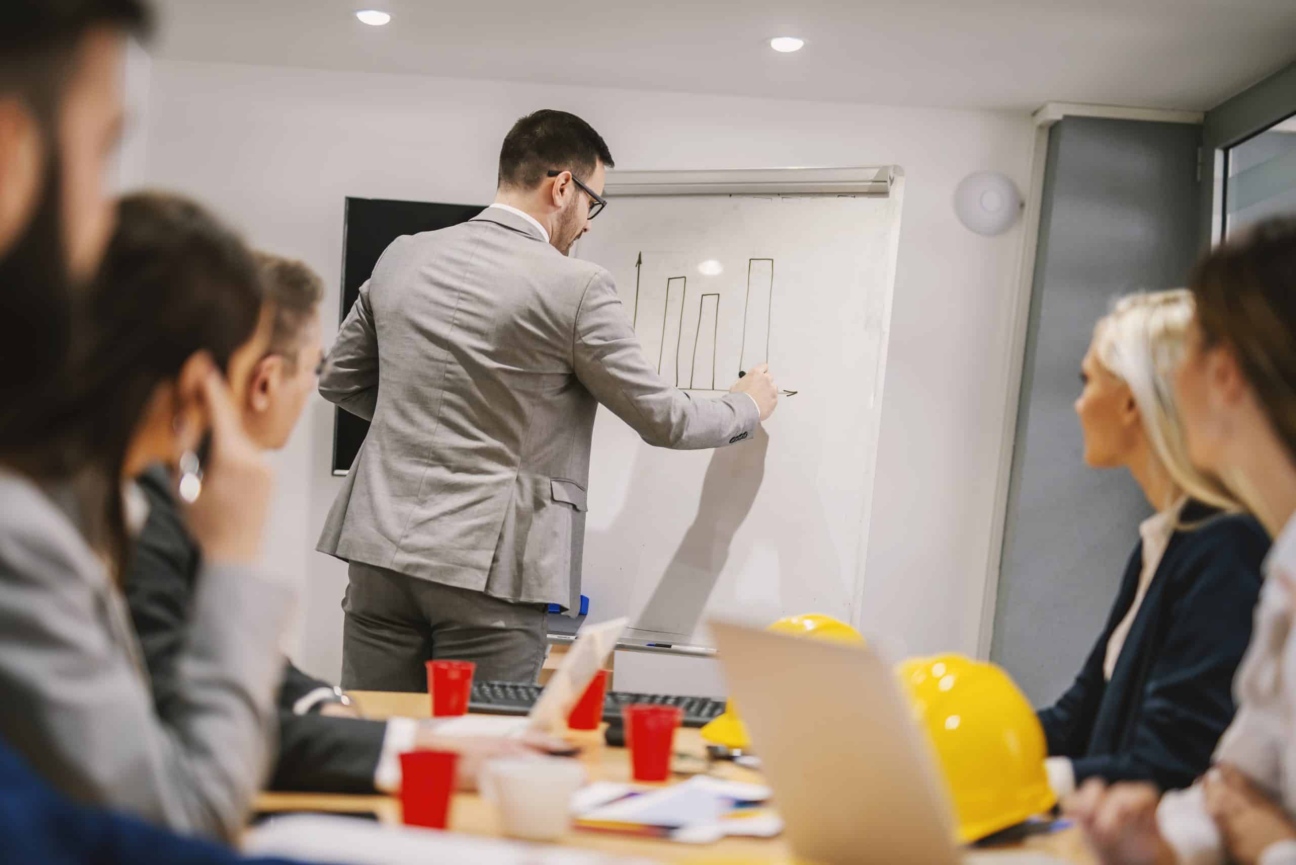 Um empresário desenhando um gráfico em um quadro branco durante uma reunião.