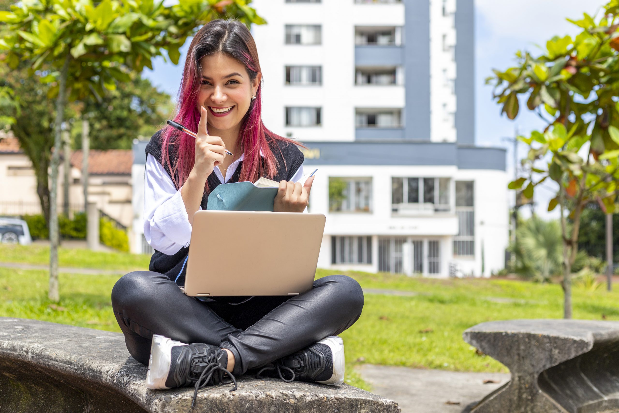 Estudante sentada na grama com um notebook fazendo anotações