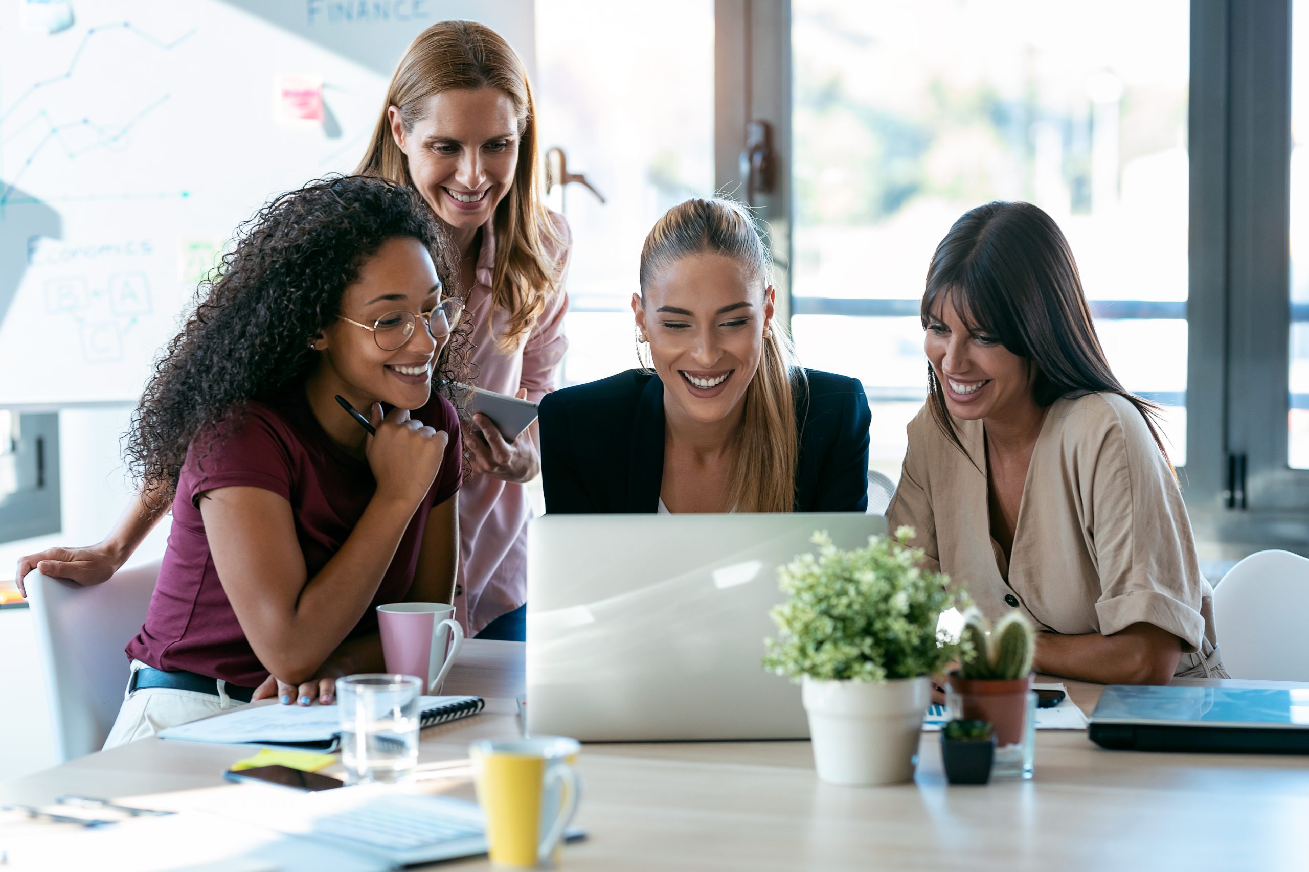 Quatro mulheres sorrindo, sentadas em frente ao computador.