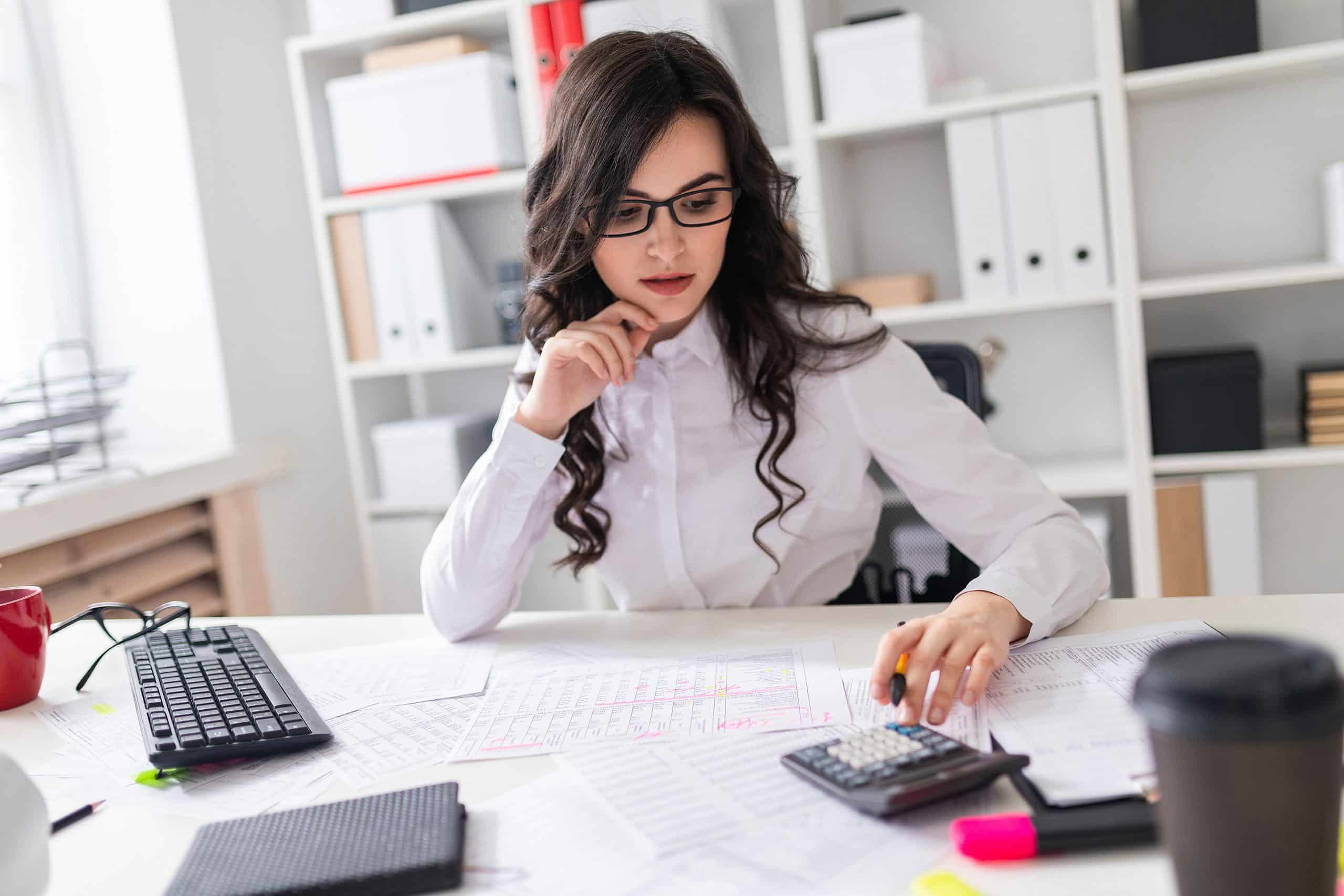 Jovem sentada em uma mesa de escritório com uma calculadora