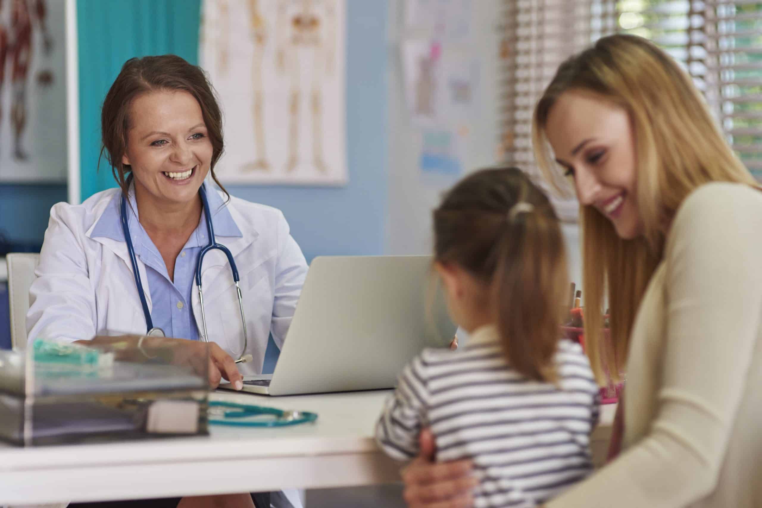 Médica conversando com uma mãe e sua filha em um consultório.