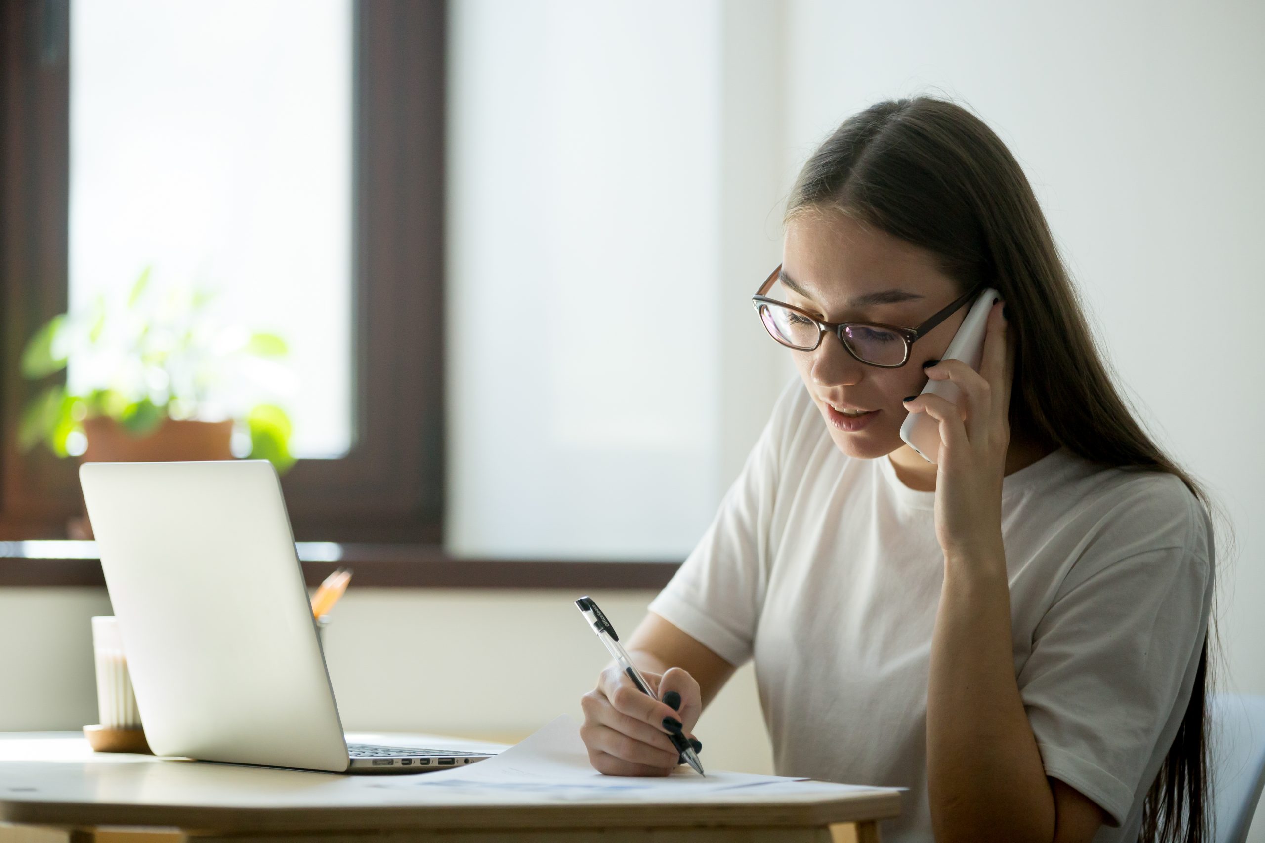 Mulher falando ao telefone e anotando em um caderno
