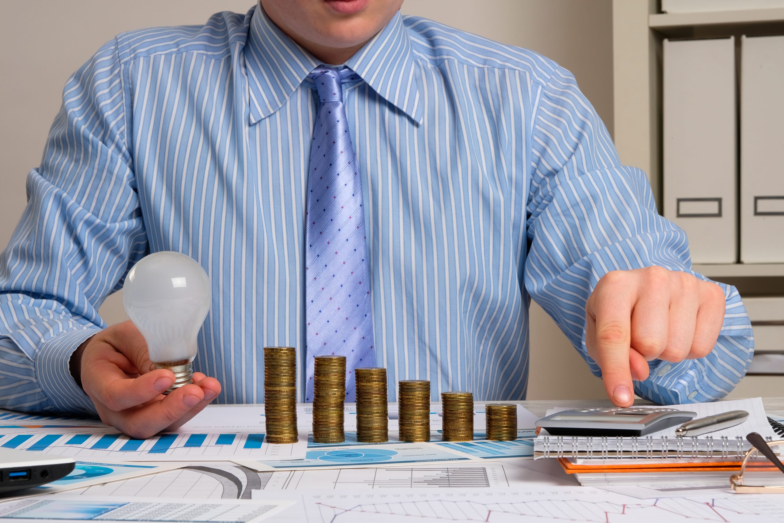 Homem trabalhando em uma mesa com papeis, moedas e uma calculadora.