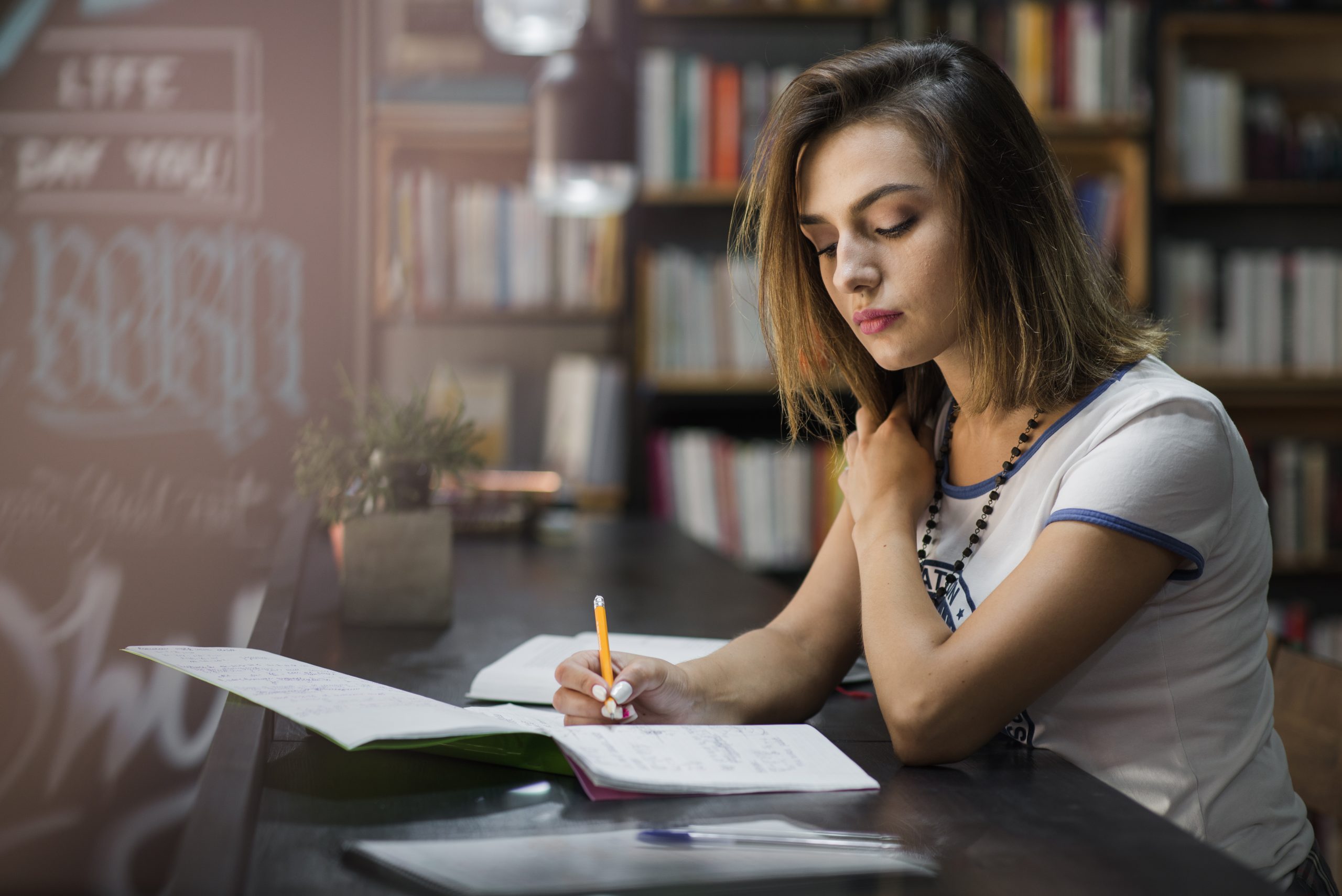 Menina sentada em uma mesa escrevendo em um caderno