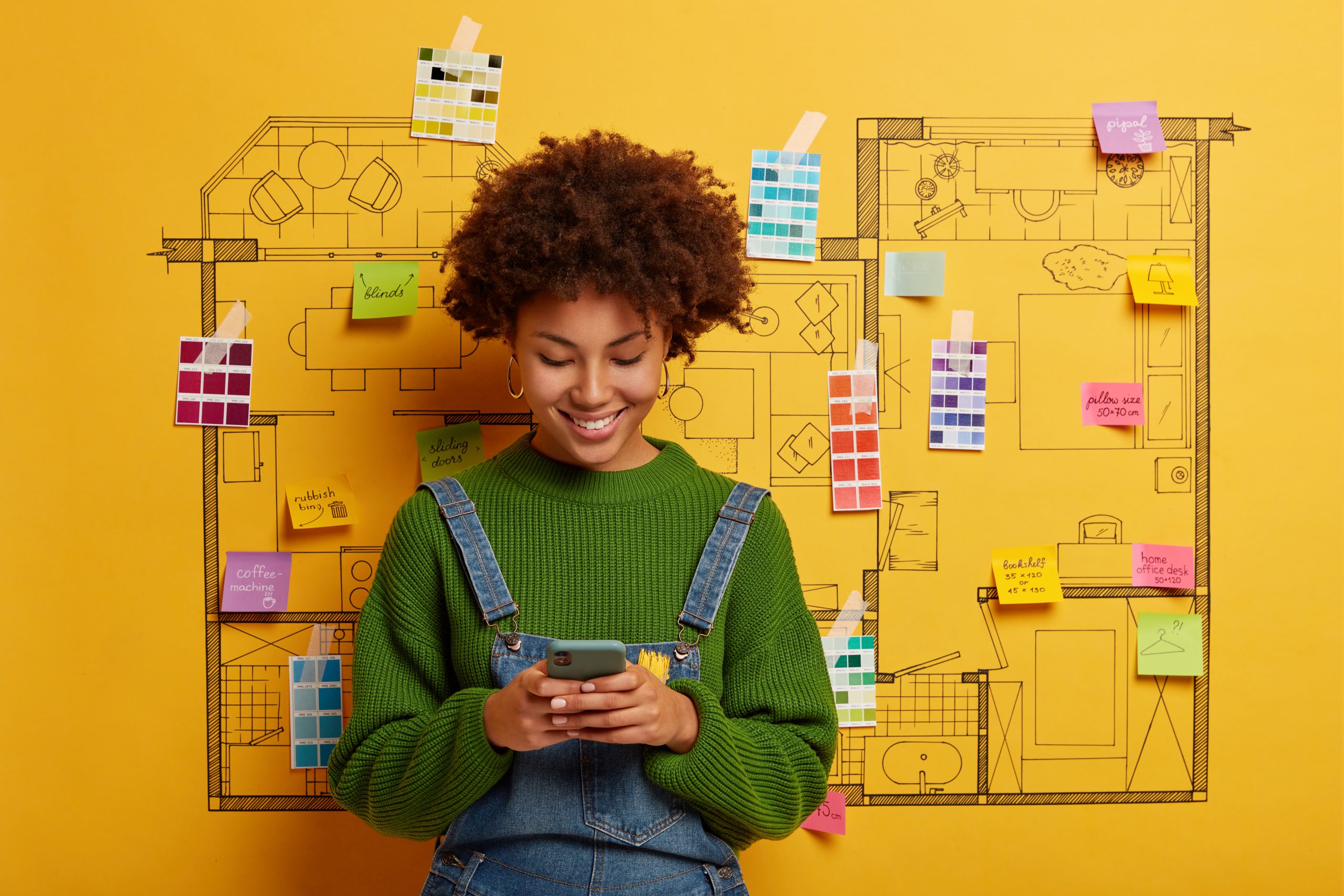 Mulher usando um celular frente a um quadro amarelo com alguns post-its.