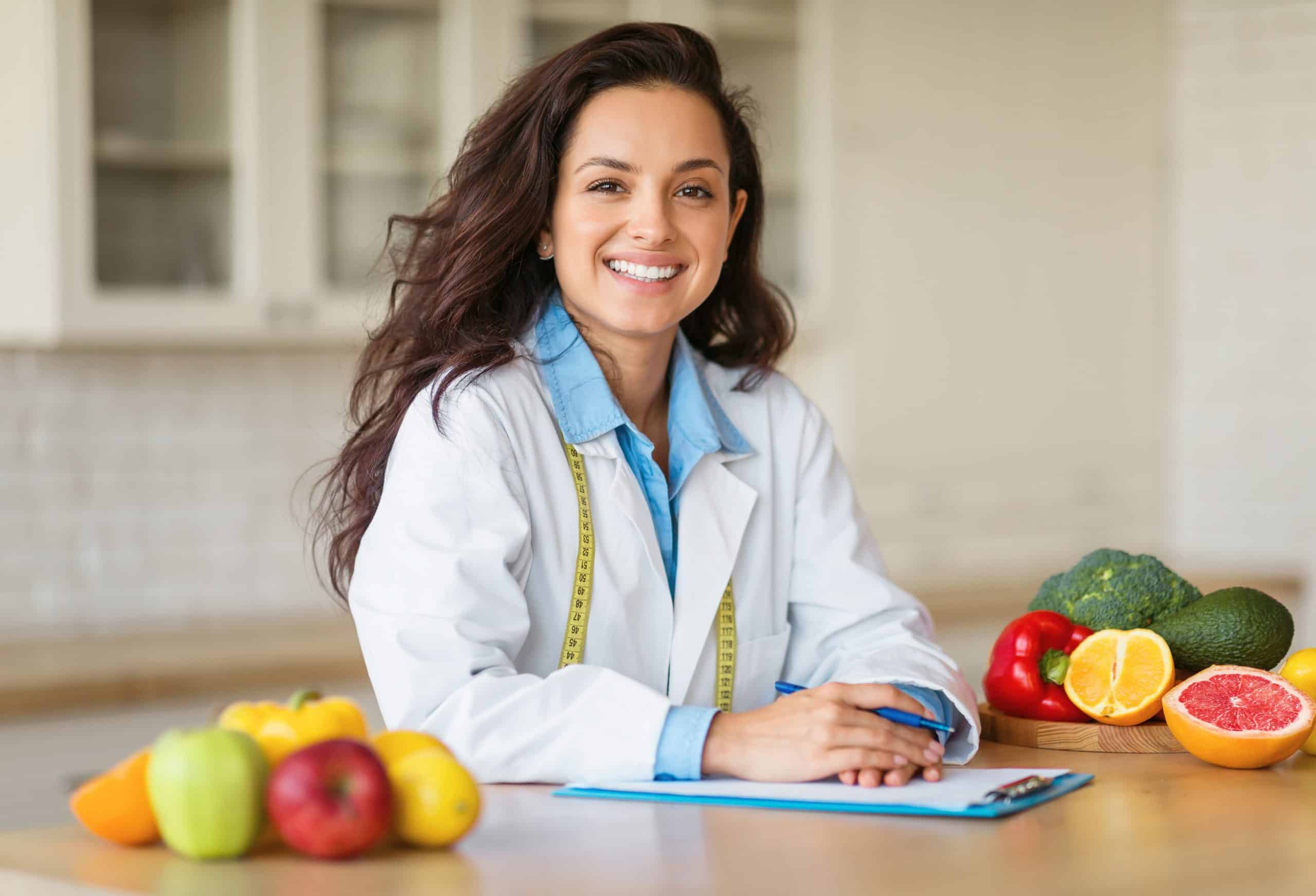 Mulher sentada em uma mesa escrevendo em uma folha com algumas frutas em volta.