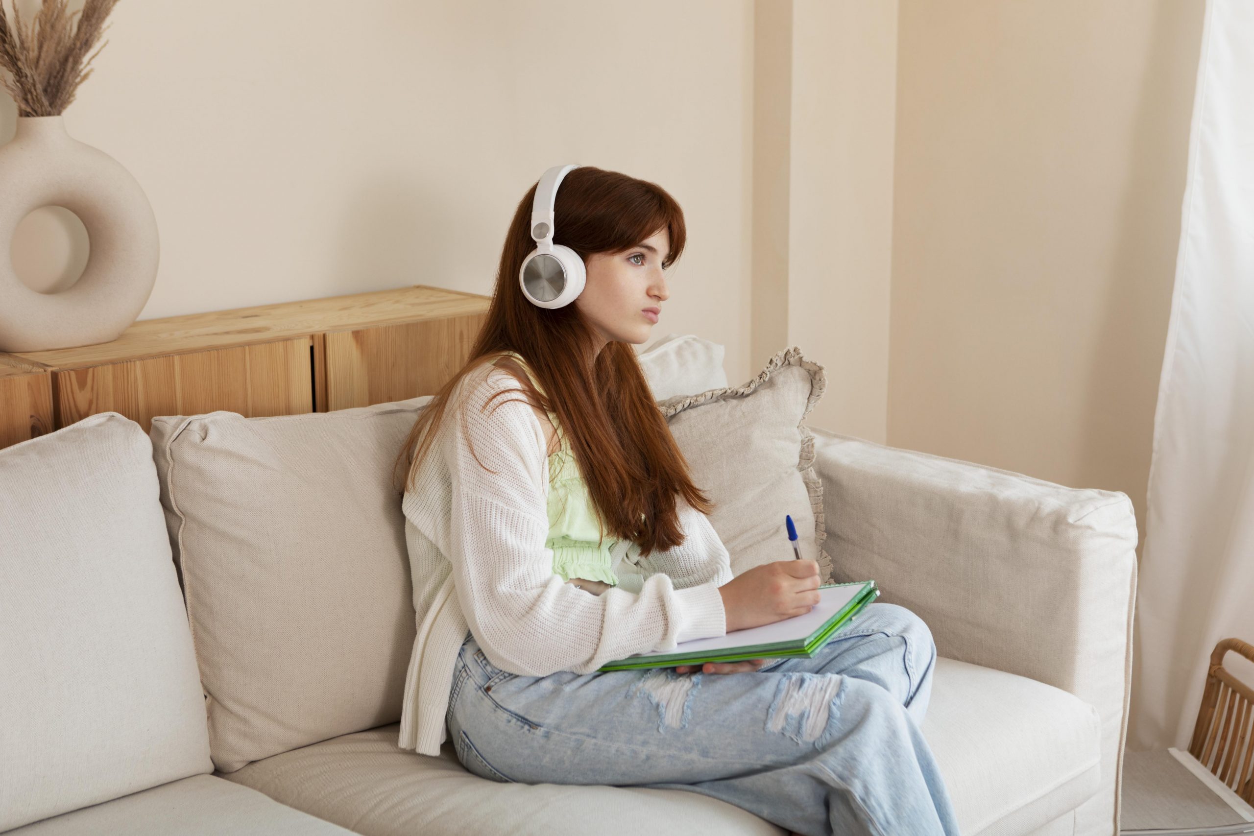 Estudante usando fones, escrevendo em um caderno