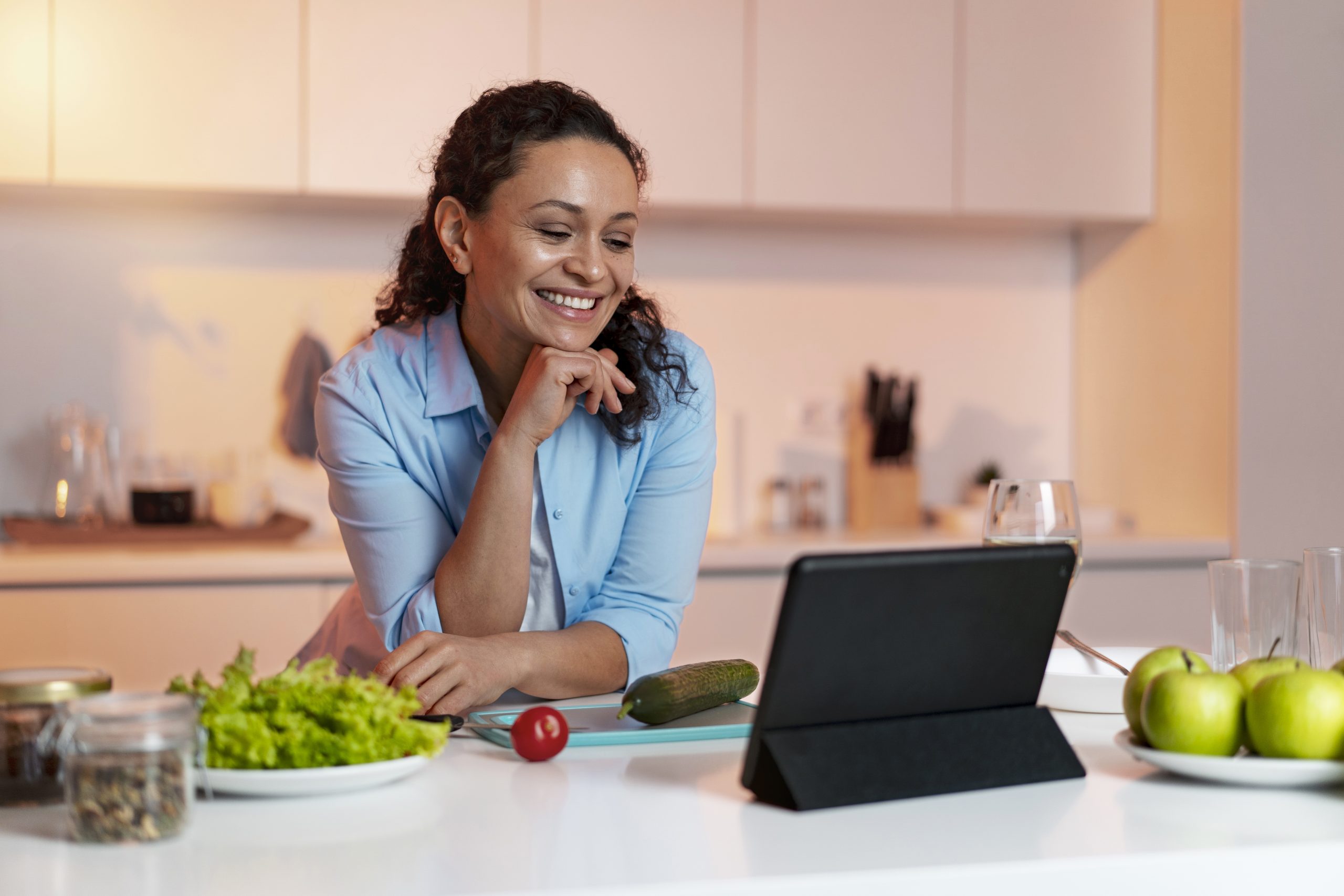 Mulher sorrindo olhando para um tablet na cozinha