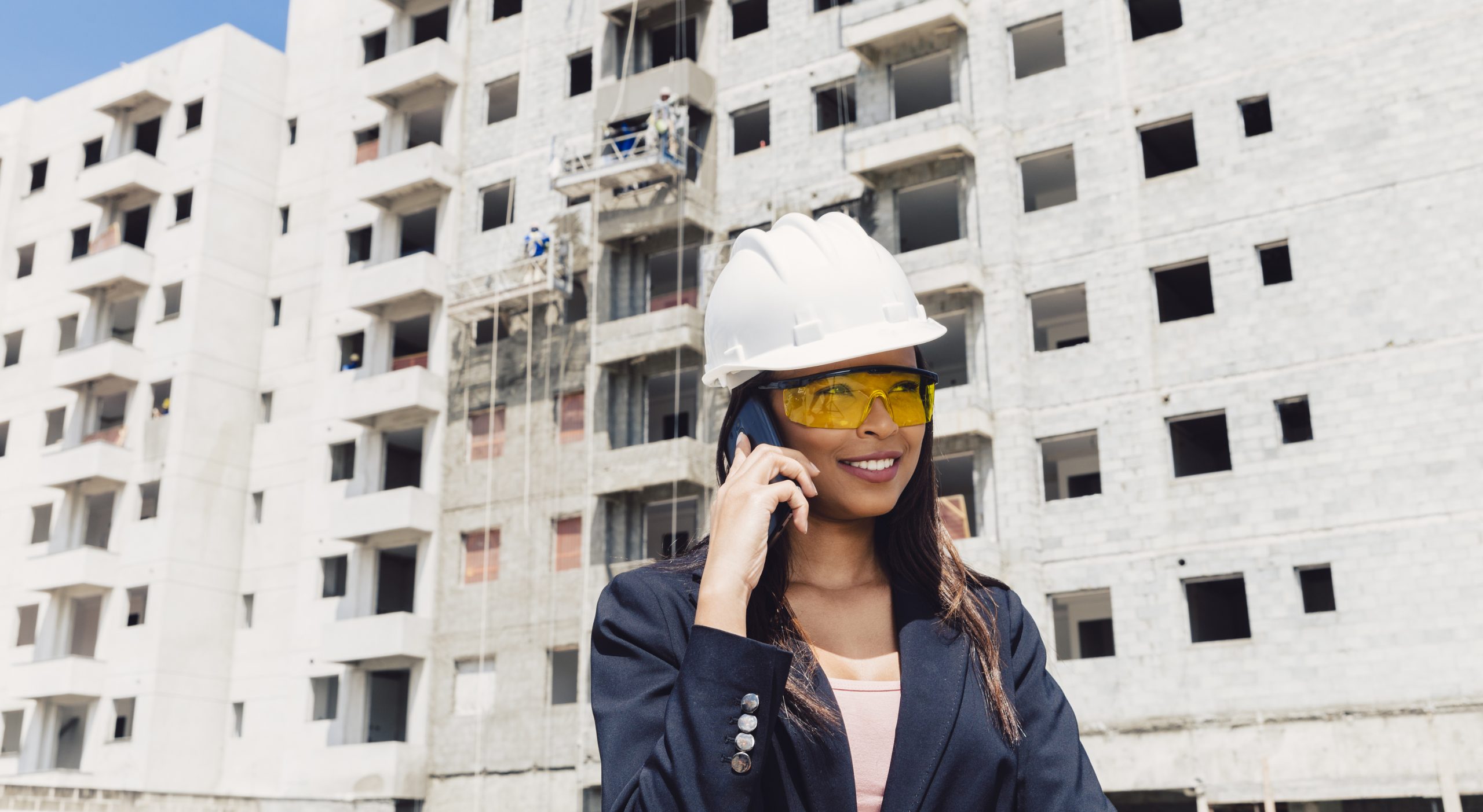 Engenheira sorrindo telefone em frente a um predio em obra