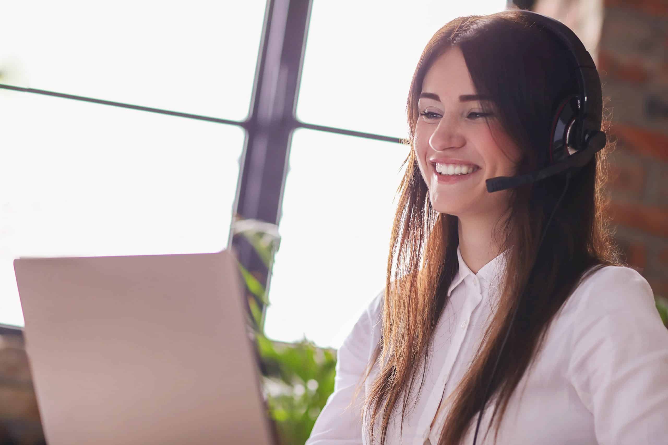 Mulher sorrindo em frente a um notebook com um headset