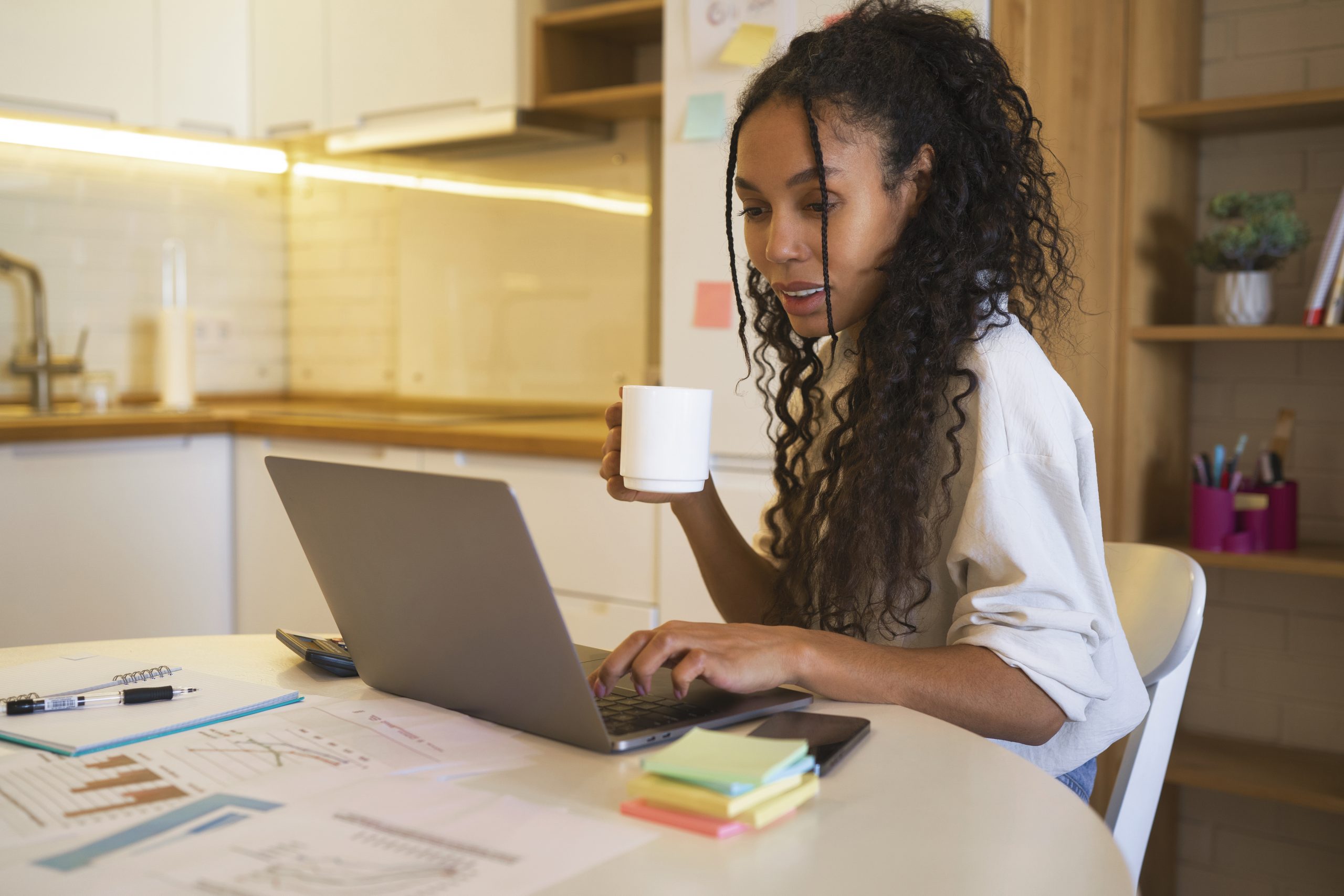 Mulher com uma xicara nas mãos, mexendo em um notebook