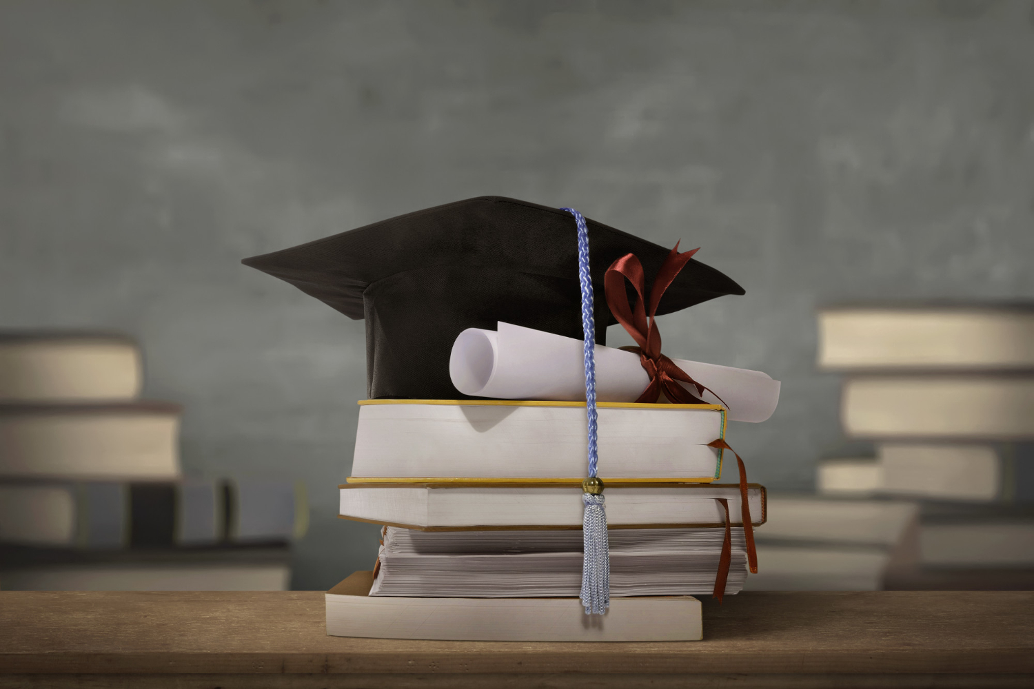 Alguns livros empilhados com um diploma e um capelo no topo