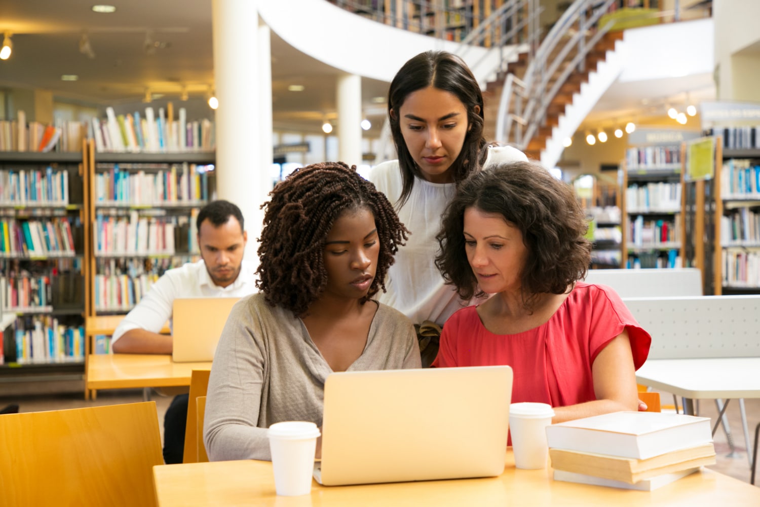 grupo de mulheres reunidas em um notebook na biblioteca