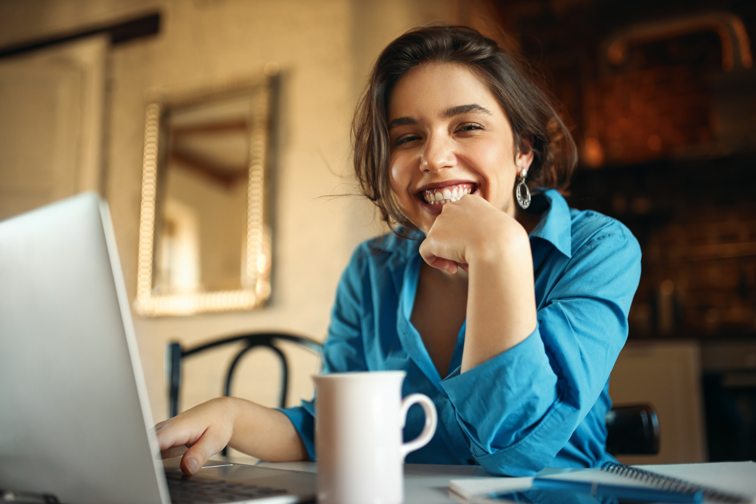 mulher sentada em frente a um notebook sorrindo para a câmera