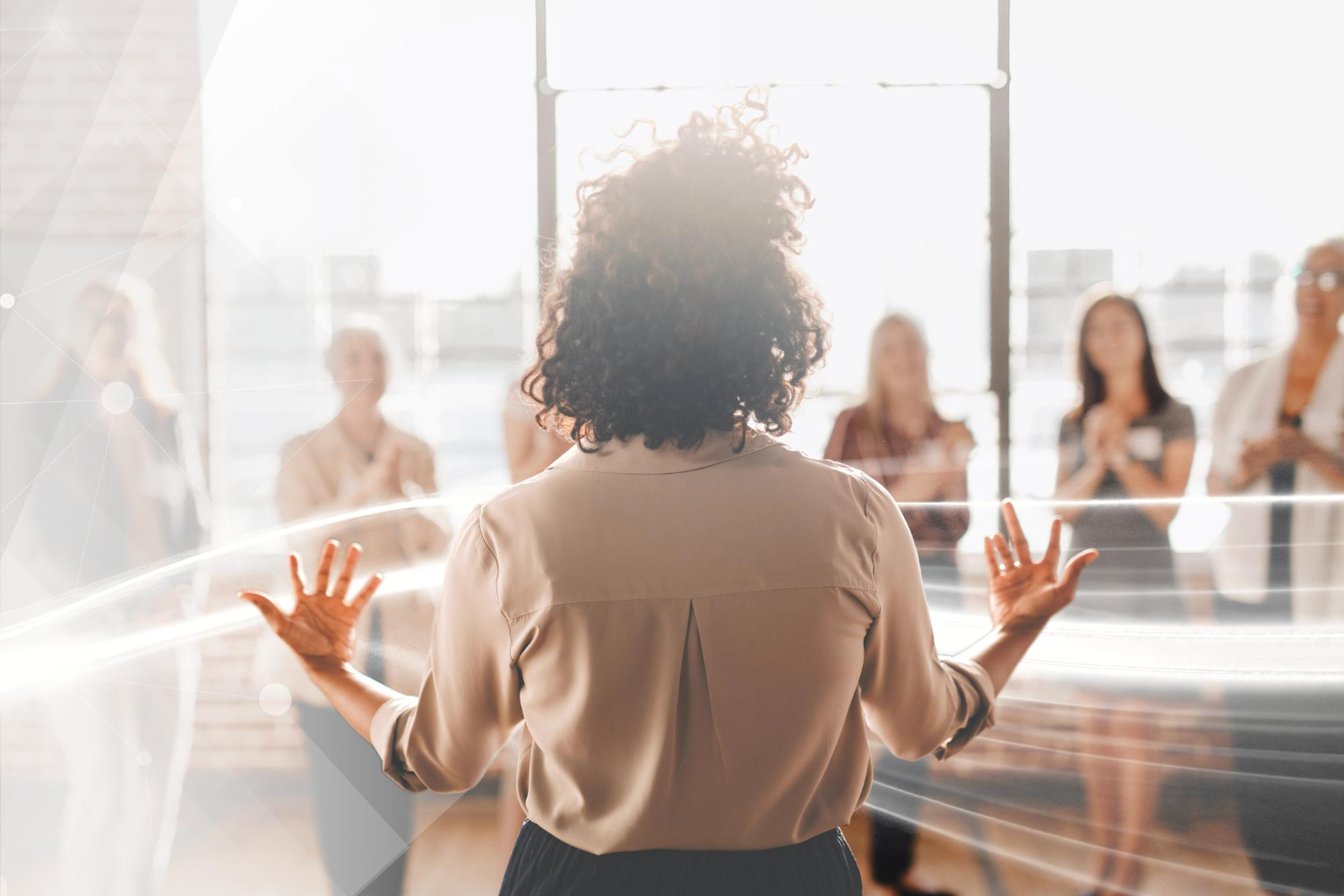 imagem de uma mulher de costas para a câmera liderando uma conversa em grupo no ambiente de trabalho